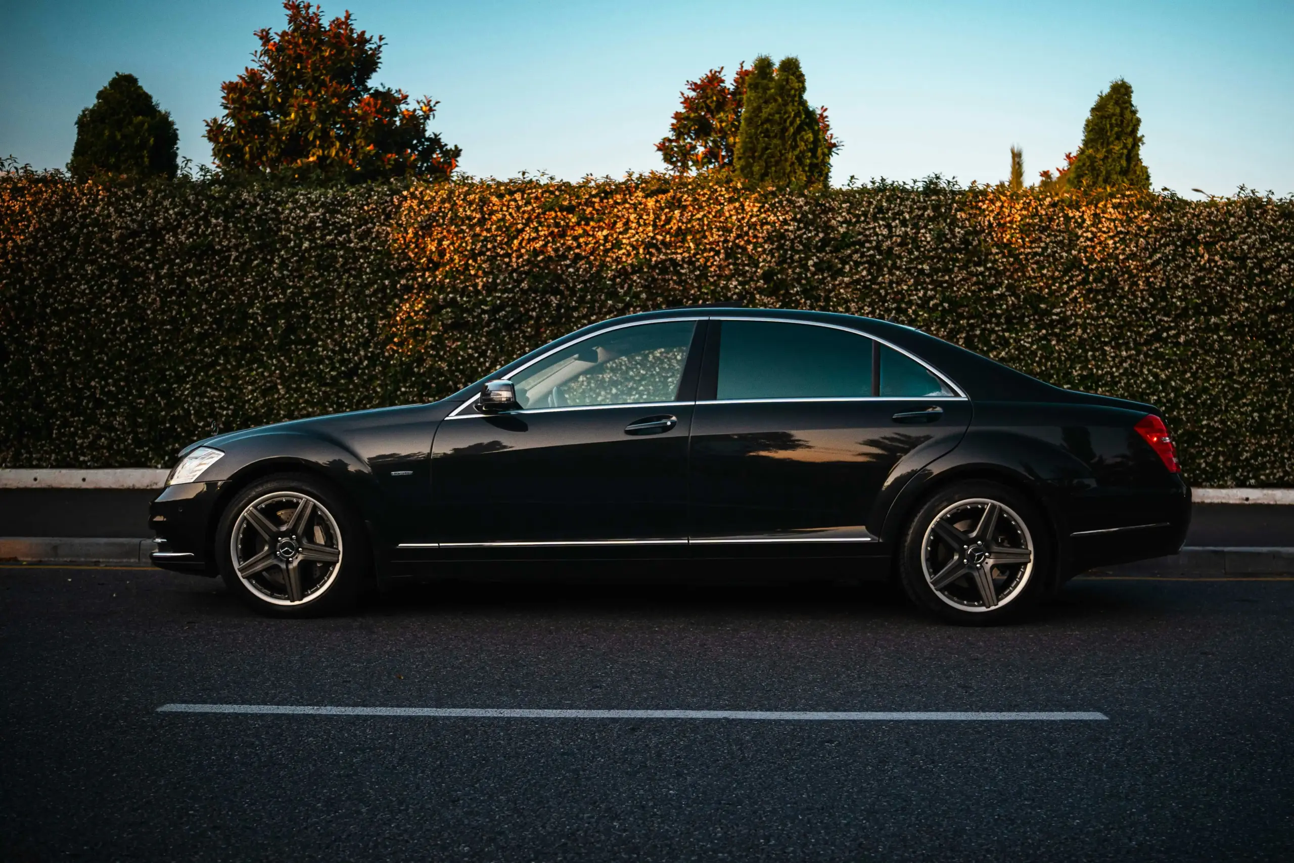 black executive sedan parked curbside in downtown Seattle at dusk with skyline reflections, wet streets, and a professional chauffeur opening the rear door