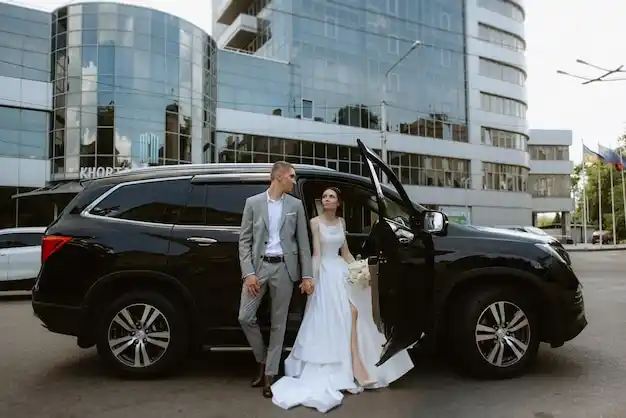 bride and groom stepping into a polished luxury vehicle outside a Seattle wedding venue with floral arrangements, soft evening light, and the Space Needle faintly visible in the...