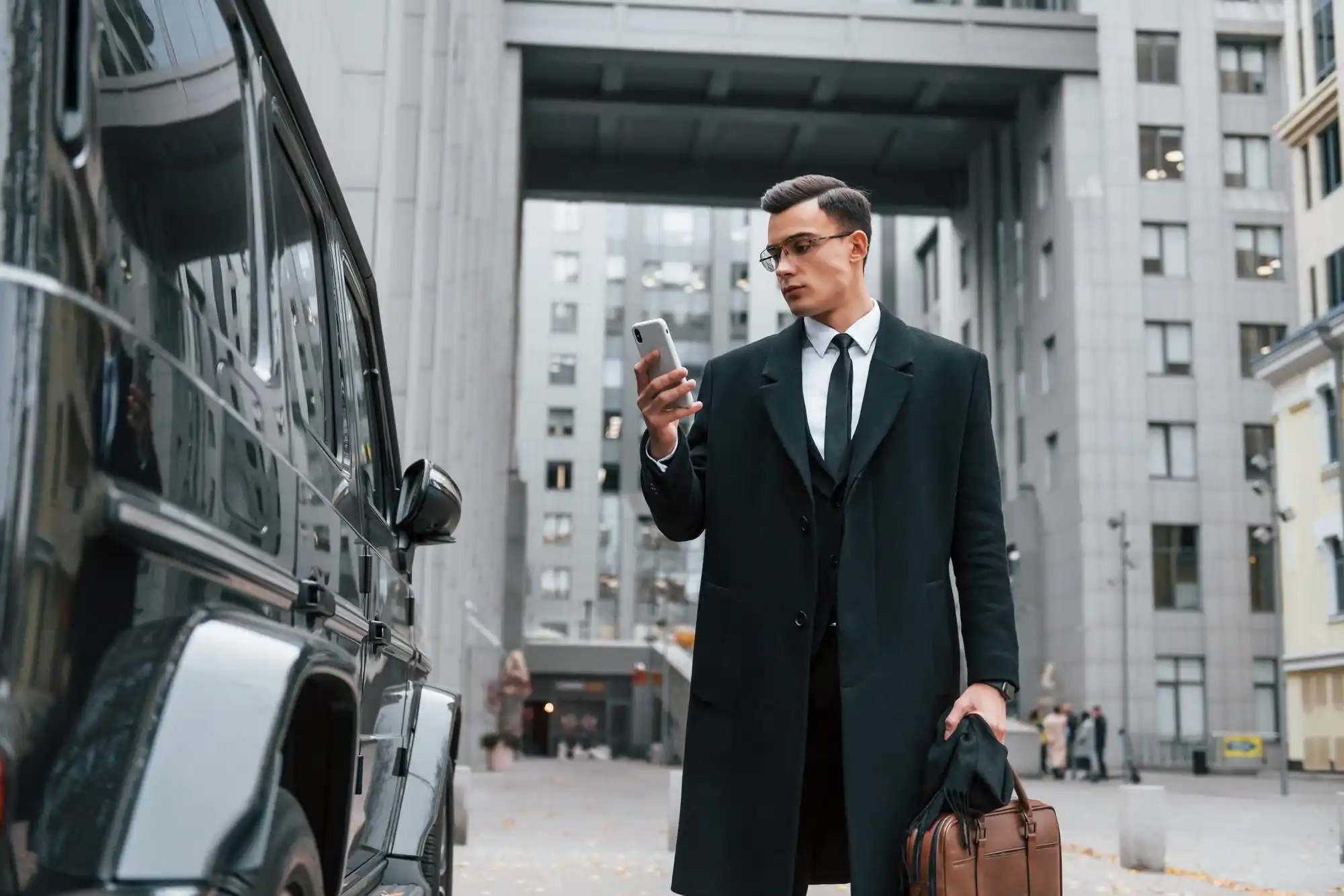 professional chauffeur in a tailored black suit standing beside a polished luxury SUV near Sea-Tac Airport arrivals, holding a name sign, overcast Pacific Northwest sky