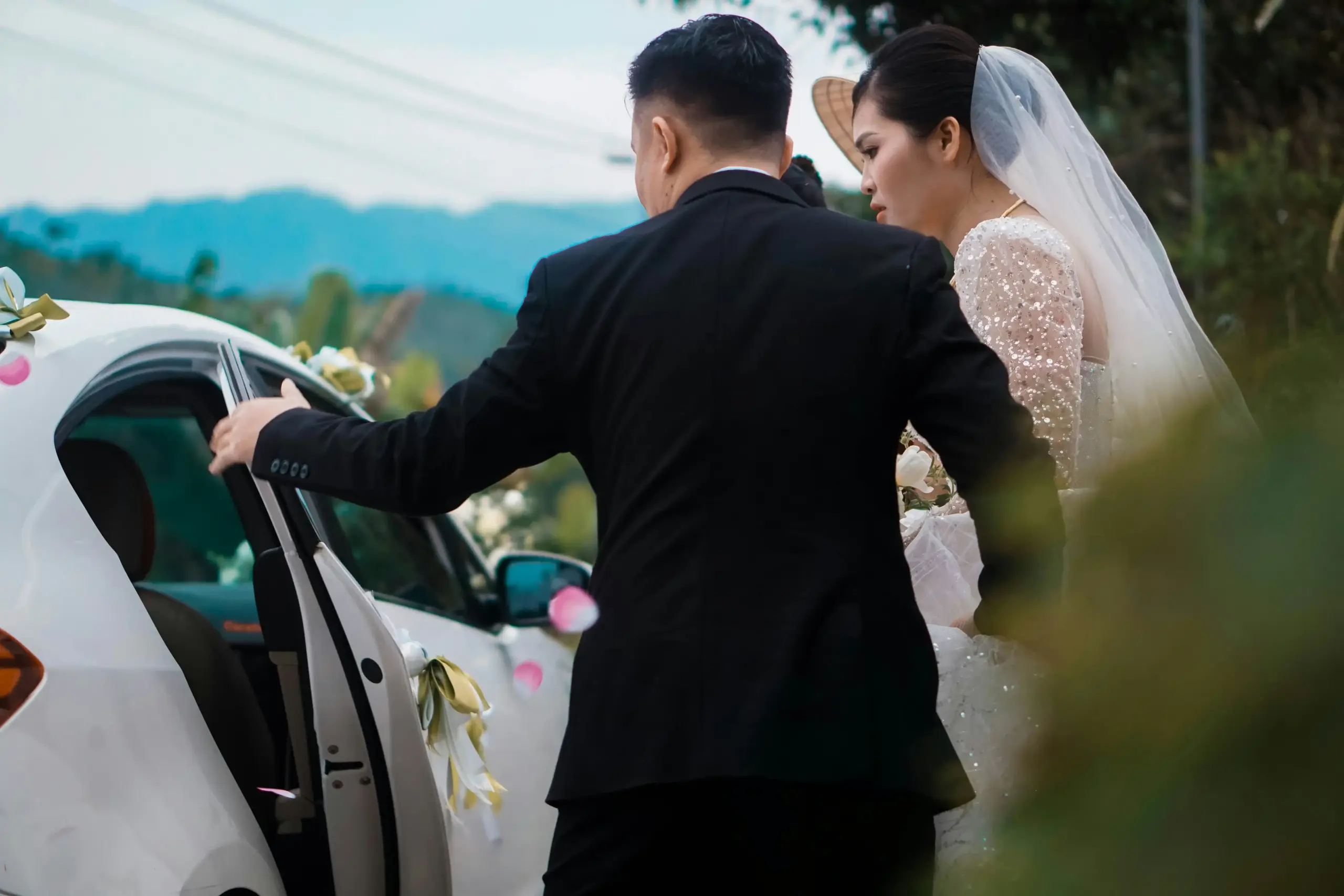 wedding couple in formal attire entering a white stretch limousine outside a Seattle waterfront venue at sunset, chauffeur assisting while guests watch