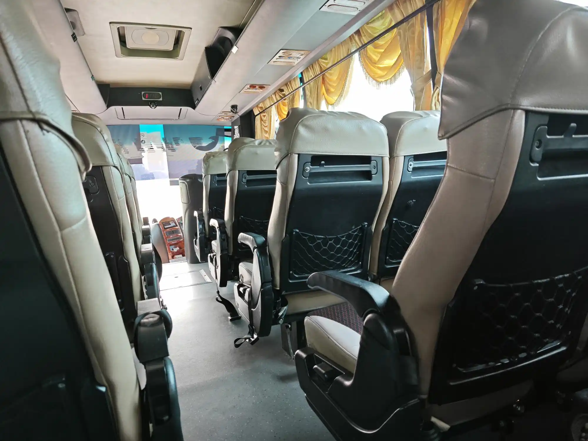 interior of a premium sprinter bus with tan leather seats, wood trim, soft LED ceiling lights, bottled water in cup holders, business presentation folders on seats
