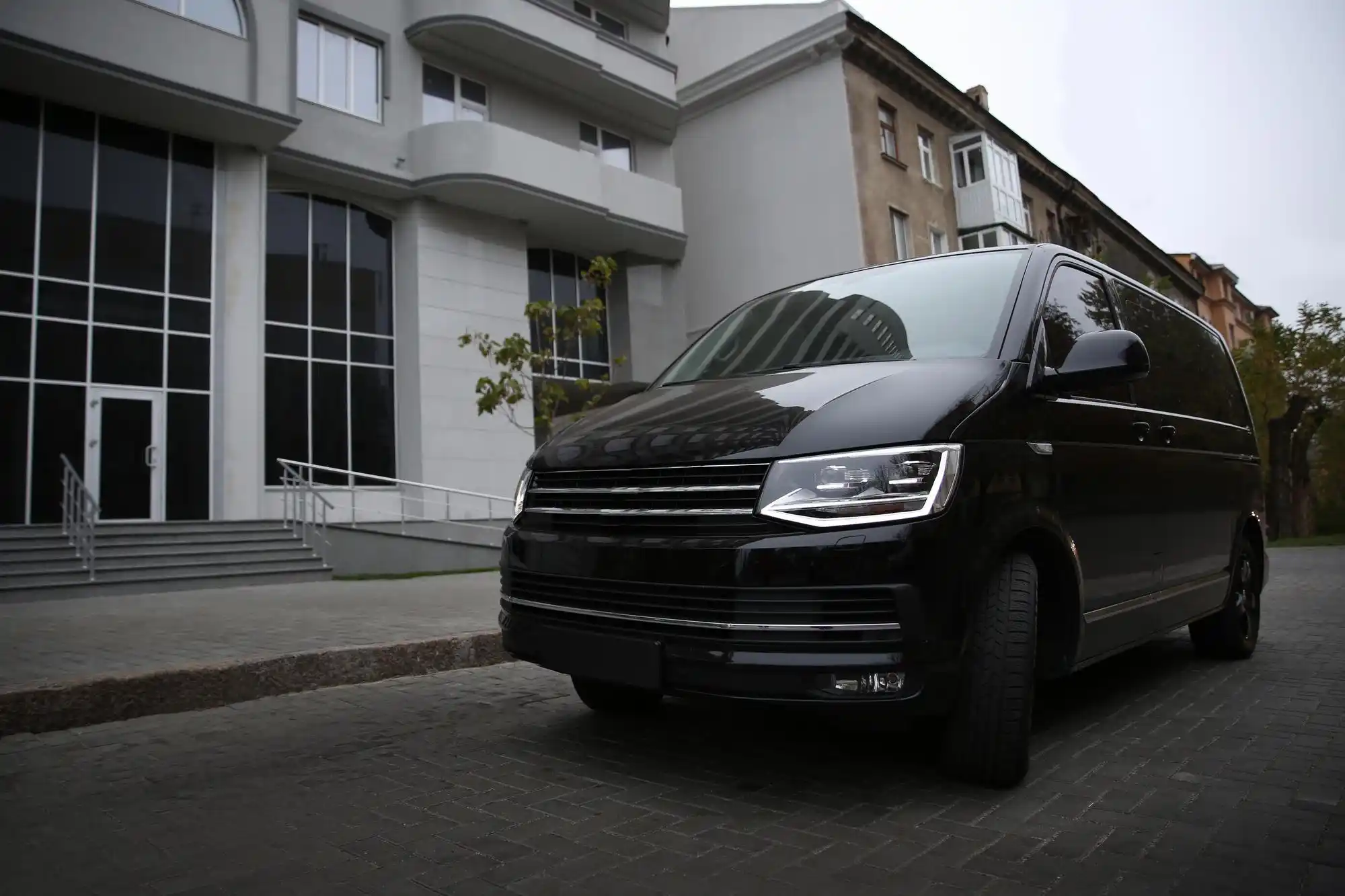black luxury Mercedes Sprinter van parked outside a modern downtown Seattle office tower on a rainy morning, executives boarding with briefcases, skyline and glass buildings in ...