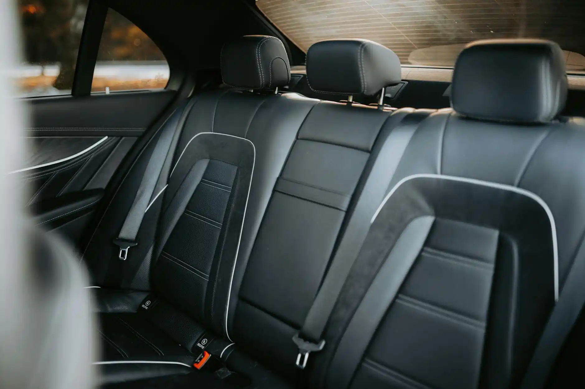 executive traveler in tailored suit inside premium black car checking flight details on smartphone, Seattle skyline reflected in window, leather interior, laptop bag and carry-o...