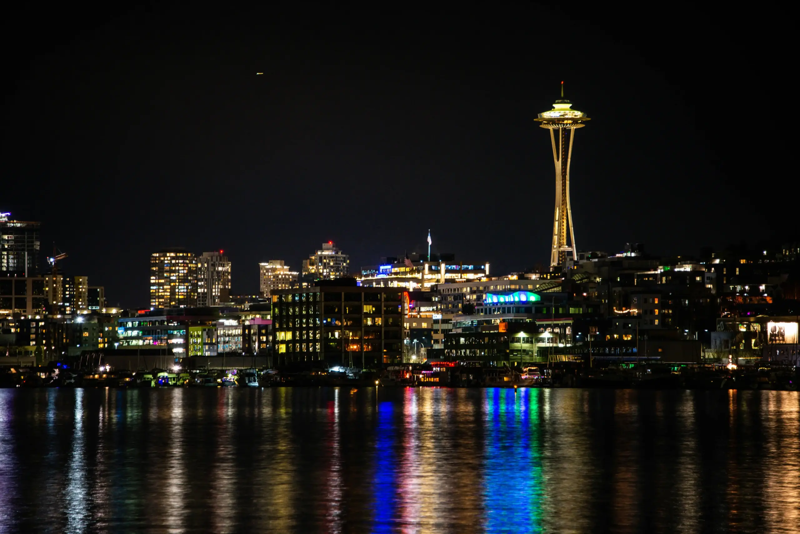 evening scene outside T-Mobile Park in Seattle with Mariners fans arriving, black luxury sedan at curbside, glowing stadium lights, light rain on pavement, downtown skyline in b...
