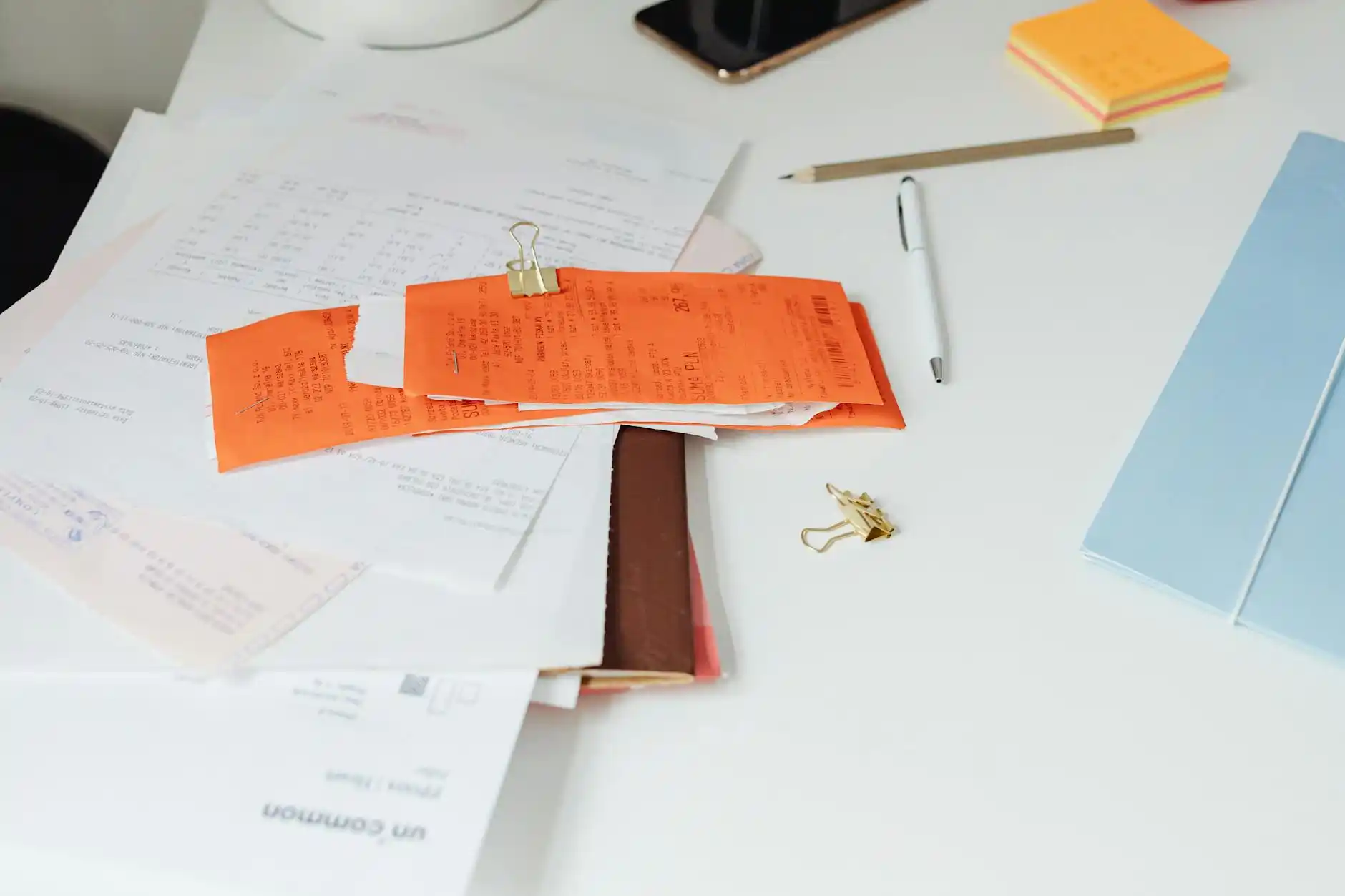 overhead view of a corporate desk with travel receipts, parking stubs, a smartphone showing rideshare surge pricing, laptop spreadsheet, and coffee cup in a busy Seattle office