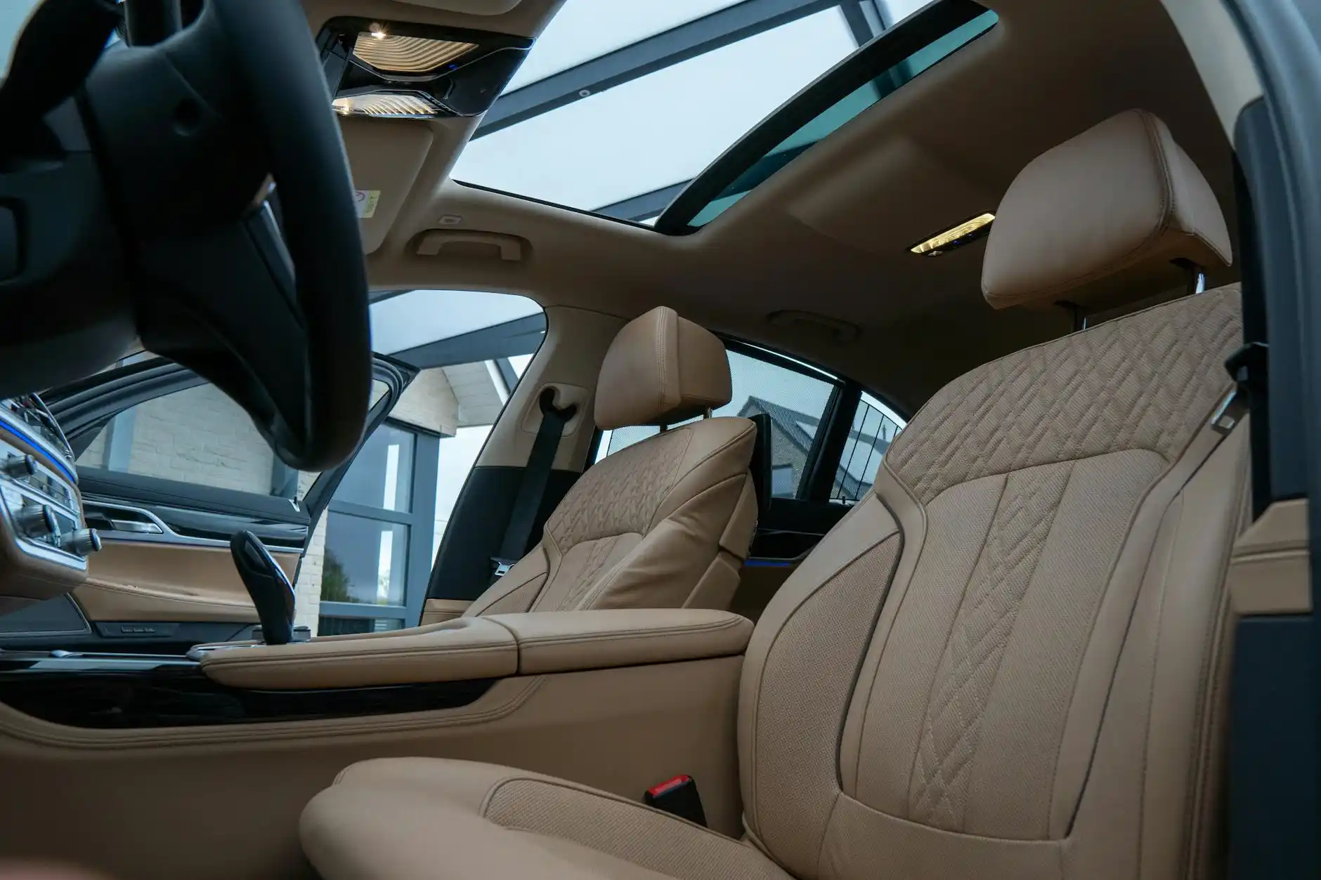 luxury black SUV interior with tan leather seats, bottled water, phone charging ports, and a laptop open with Seattle skyline visible through tinted window