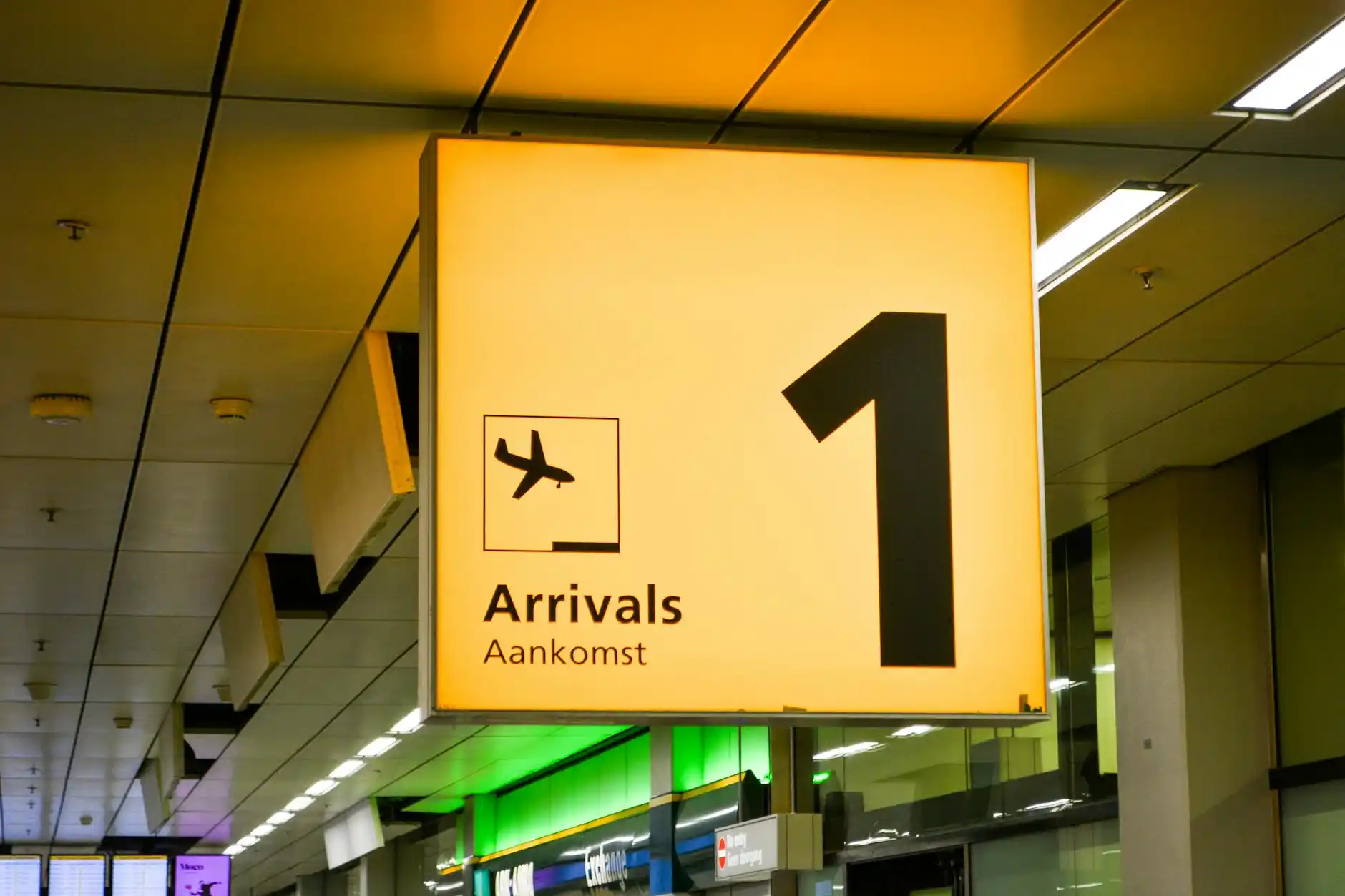 black luxury sedan waiting at Seattle-Tacoma International Airport arrivals curb at dusk, chauffeur holding digital name sign, traveler with carry-on approaching under terminal ...