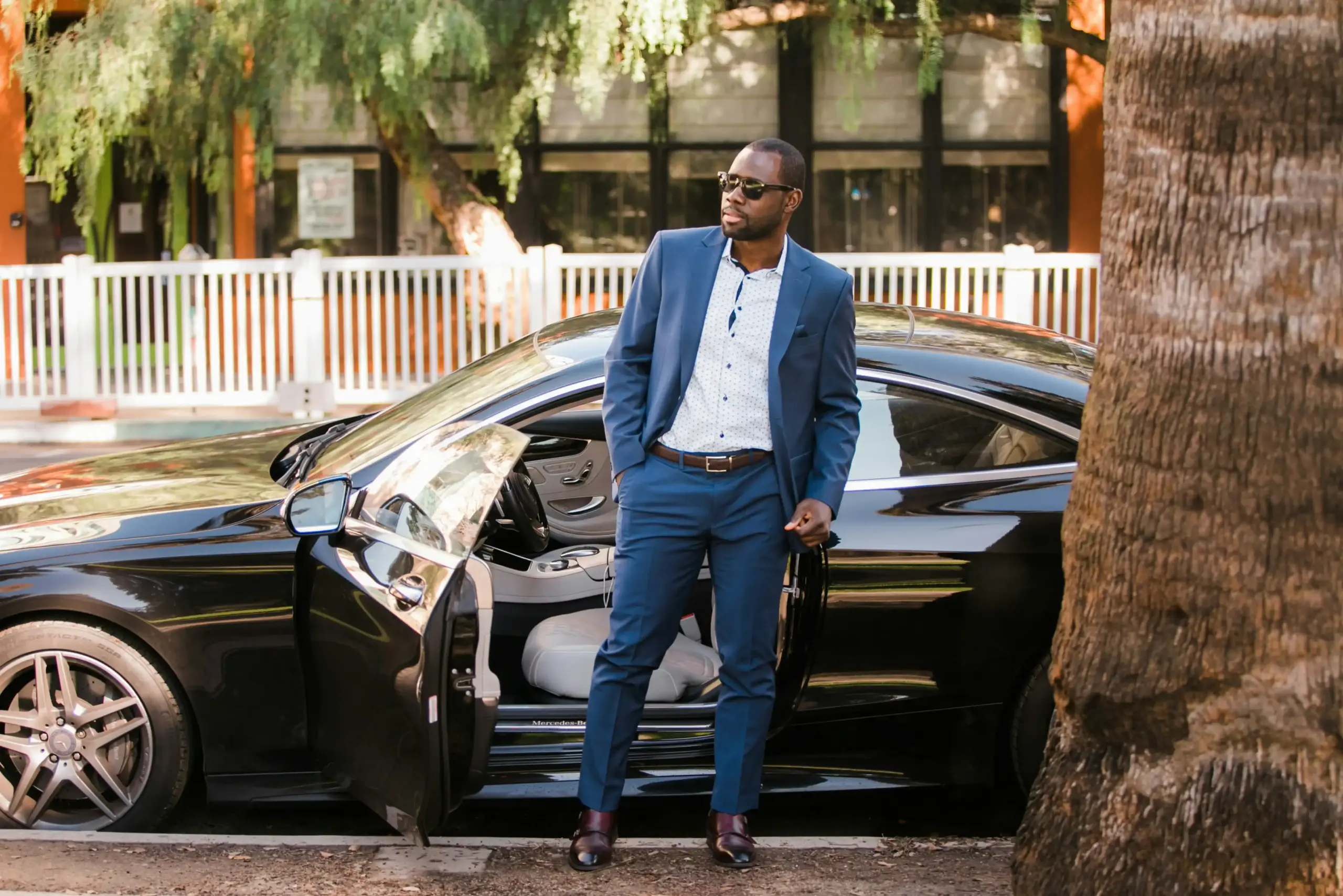 professional chauffeur in dark suit greeting hotel guest beside a black sedan outside a luxury Seattle hotel entrance, bell cart with luggage nearby, morning business travel atm...
