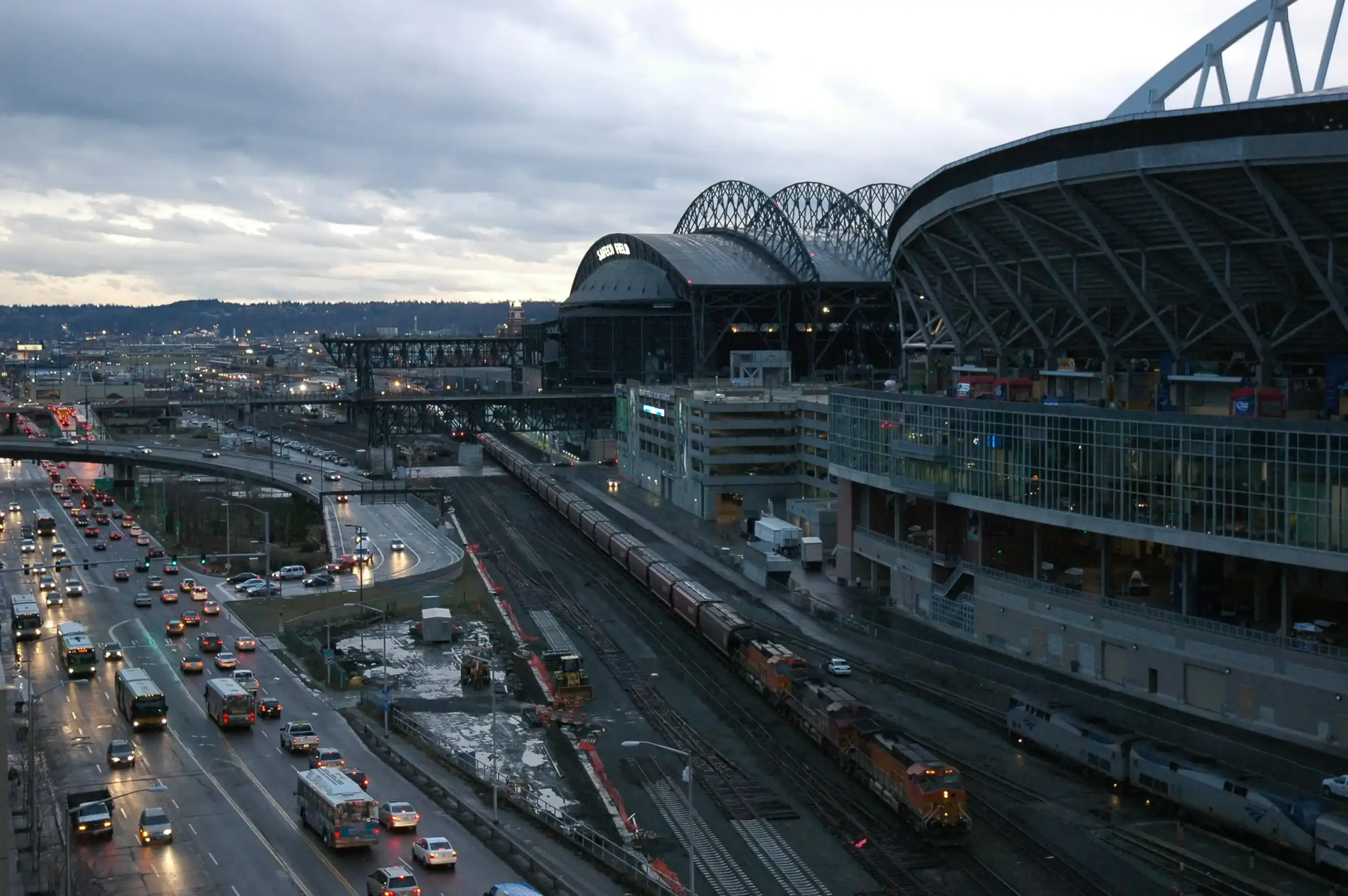 glossy black luxury sedan parked at Seattle-Tacoma International Airport curbside on a rainy evening, city lights reflecting on wet pavement, professional chauffeur opening the ...
