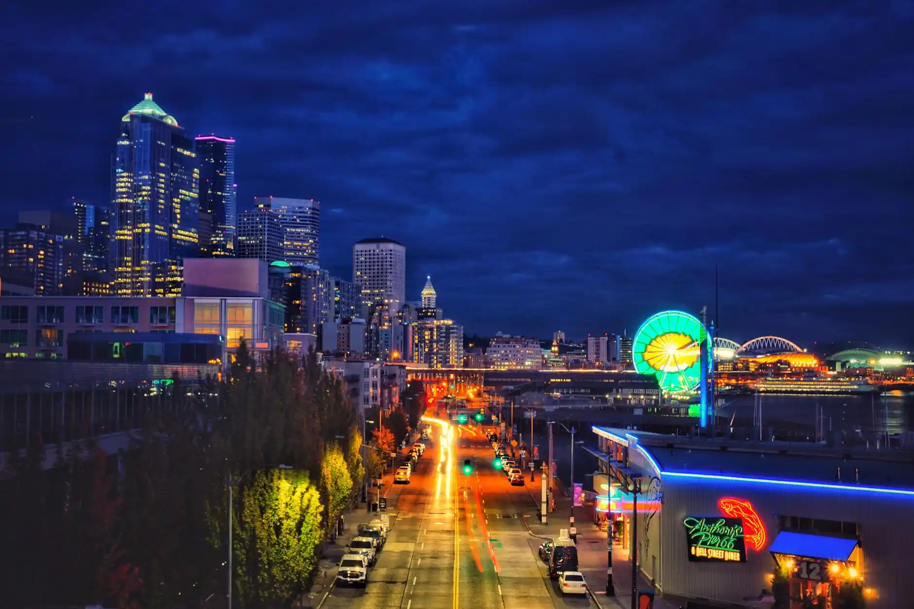 traveler in downtown Seattle at night looking anxiously at phone beside packed suitcase, empty street with light rain and blurred city traffic in background
