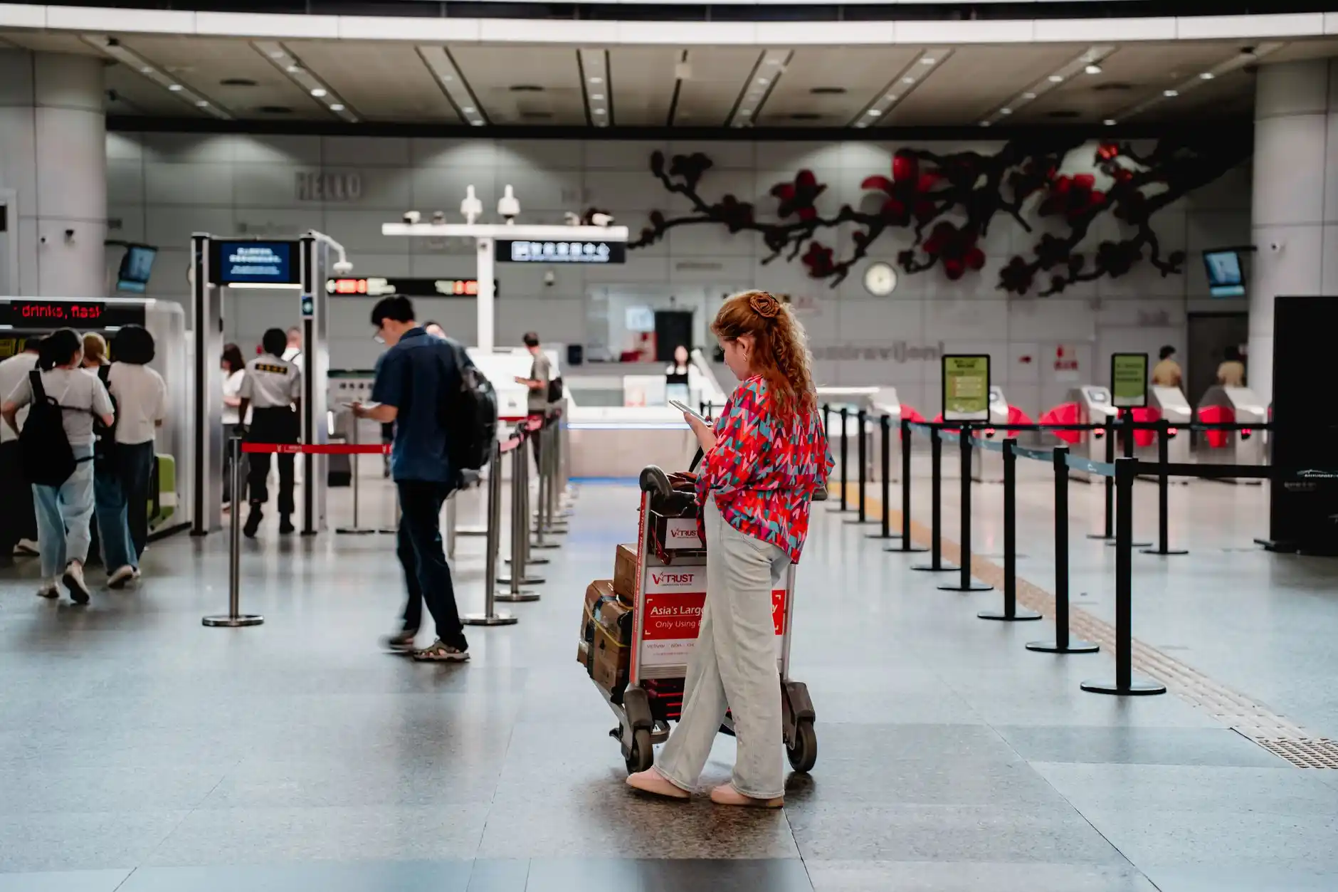 traveler checking phone beside luggage near SeaTac pickup signage while a chauffeur in professional attire waits near a luxury sedan under covered terminal lighting