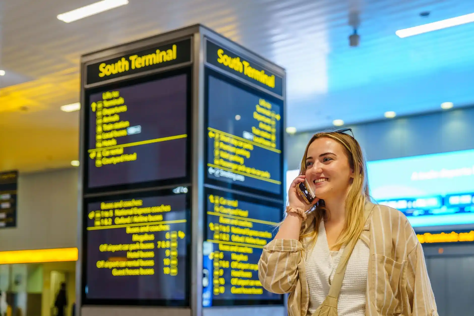traveler at airport arrivals holding phone with clear pickup text message, black SUV waiting in designated rideshare zone, overhead terminal signage visible