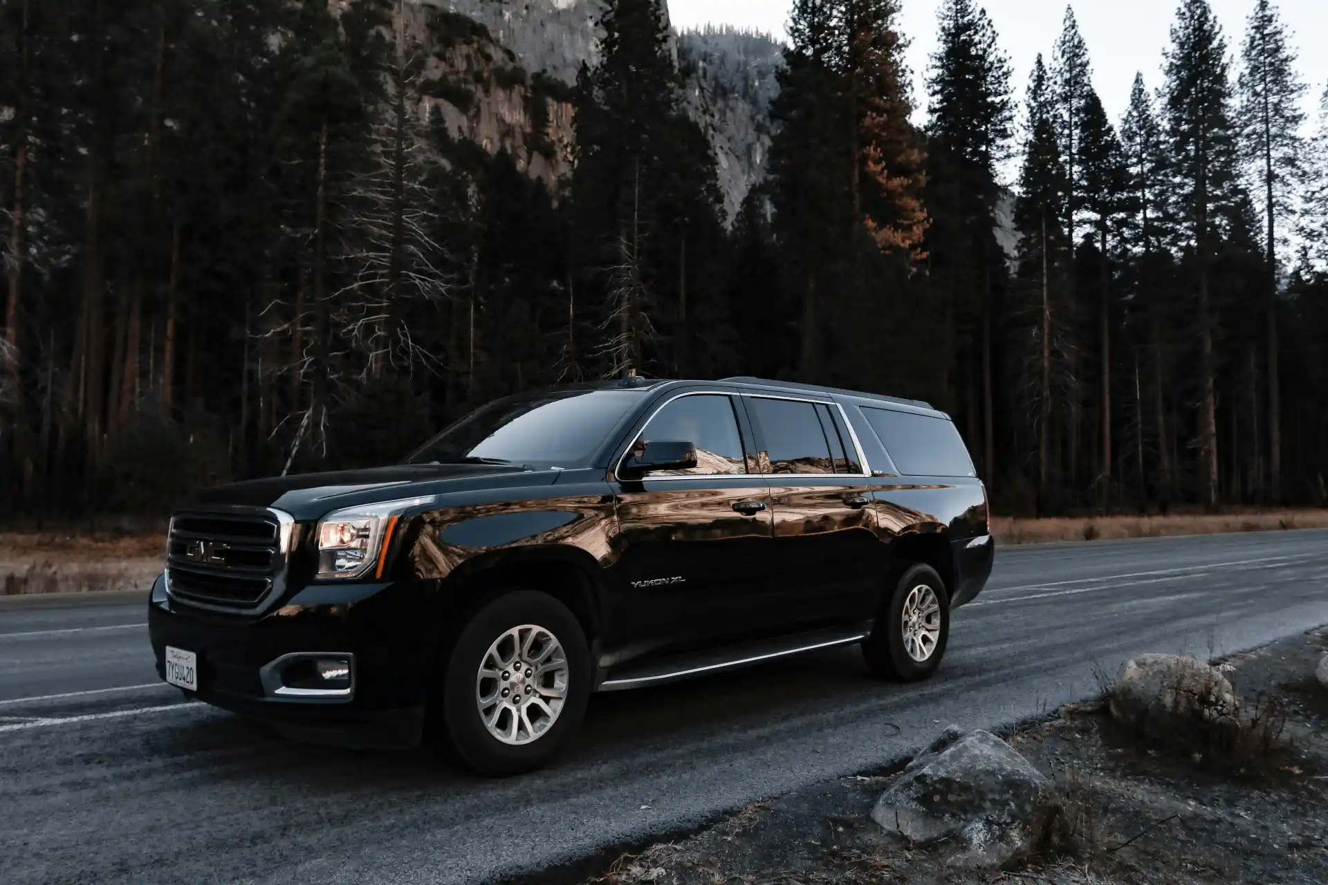 Evening pickup outside Seattle-Tacoma International Airport, professional chauffeur beside a polished black SUV holding a passenger name sign, terminal lights and travelers in t...