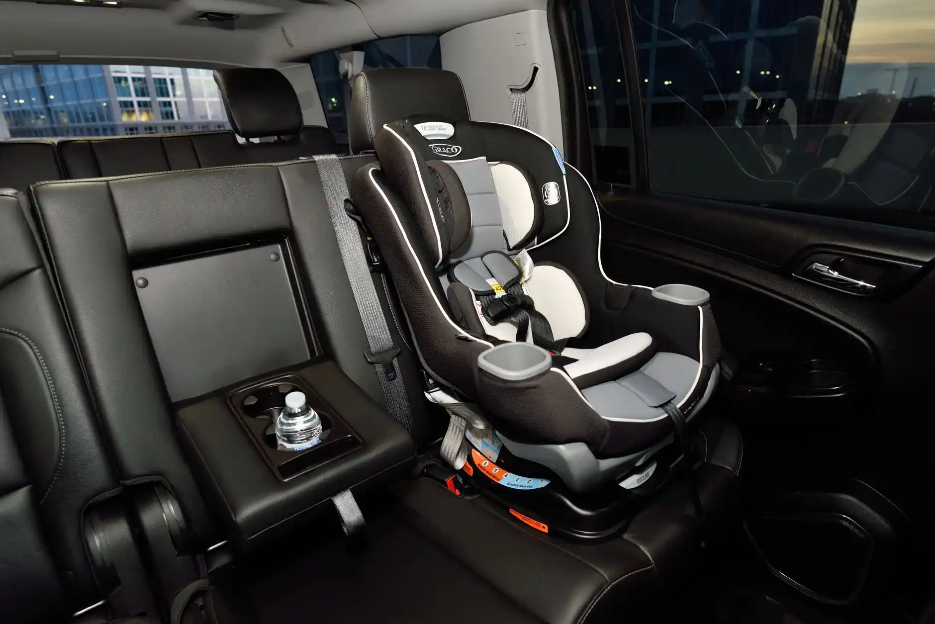 Open rear cargo area of a luxury black SUV at SeaTac showing four large suitcases, two carry-ons, and a child safety seat with ample organized space