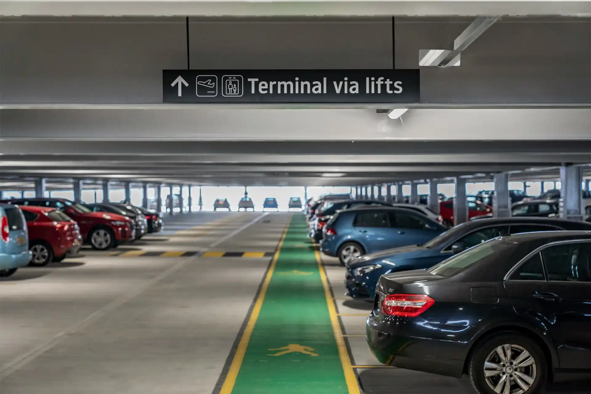 Detailed SeaTac Airport parking garage pickup area with travelers following rideshare and ground transportation signs while a chauffeur checks a flight arrival
